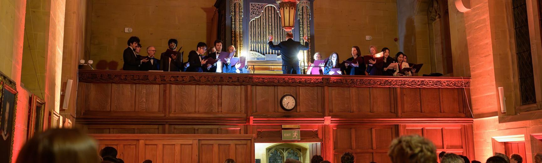 The Choir singing on the gallery above the dining hall with organ in background