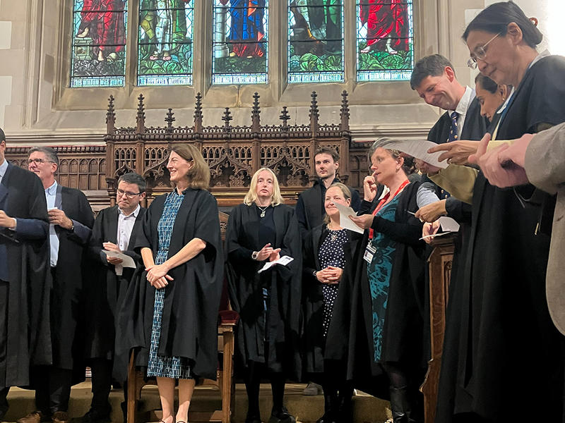 A group of people in academic gowns surround Principal Beth Breeze in the College Chapel