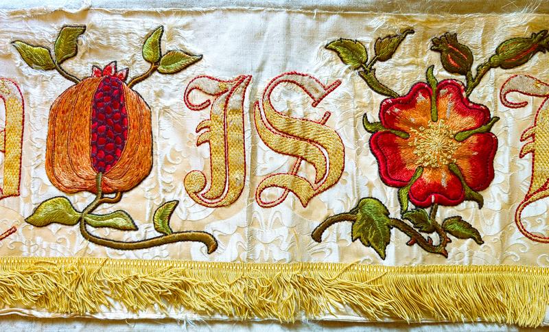 Detail of an embroidered cloth with a piece of fruit and flower shown alongside the word IS