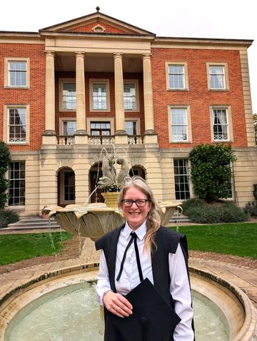 Woman in academic gown in front of a fountain, with building in the background