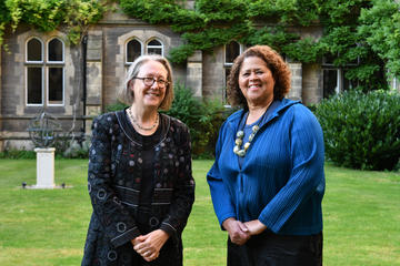 The Principal and Anna Deavere Smith smiling together in the Tate Quad. In the background, stonework, grass and green foliage