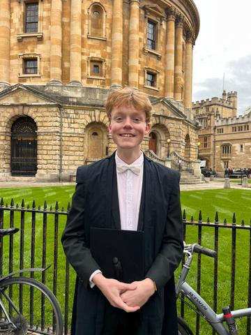 Photo of student in academic sub fusc in front of historic Radcliffe Camera building 