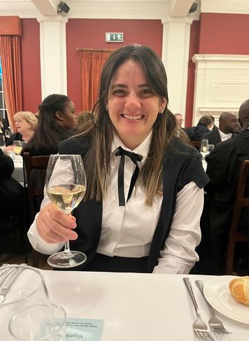 A woman in academic gown drinking a glass of wine