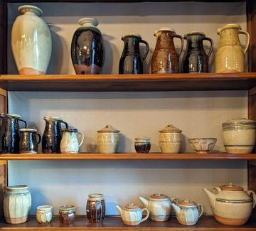 Three shelves of pottery on display in a range of shapes from jugs to teapots to jars.  