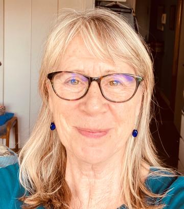 Portrait photo of Claire MacDonald. Claire wears glasses, blue drop earrings and has long hair. She is smiling directly at the viewer. 
