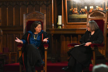 The Principal and Anna Deavere Smith are seated together in high-backed chairs at the front of the Chapel. Anna is on the left, gesturing as she explains a point, while the Principal (on the right) listens attentively. 