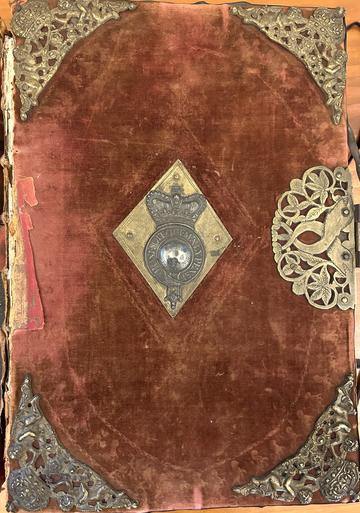 An elaborate cover with metal corners and central crest on a pink velvet background