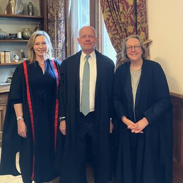 Three people, two women, one man in the centre, pose in academic gowns in a wood-panelled room