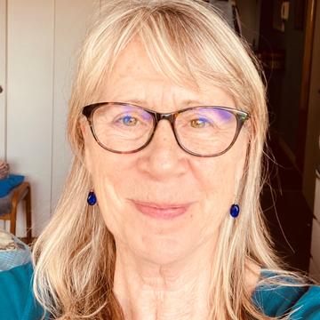 Portrait photo of Claire MacDonald. Claire wears glasses, blue drop earrings and has long hair. She is smiling directly at the viewer. 