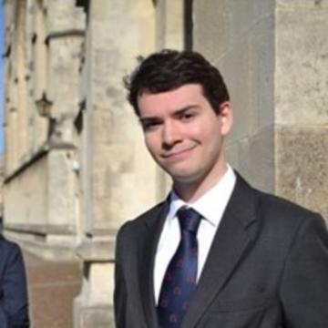 Photograph of Nicholas Stone in Radcliffe Square wearing a suit and tie and smiling at the camera. 