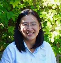 Photo portrait of Professor Bee Wee, smiling against a backdrop of green foliage