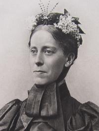 Picture of a women (headshot) with smiling with a headress with flowers and dressed in black victorian clothes