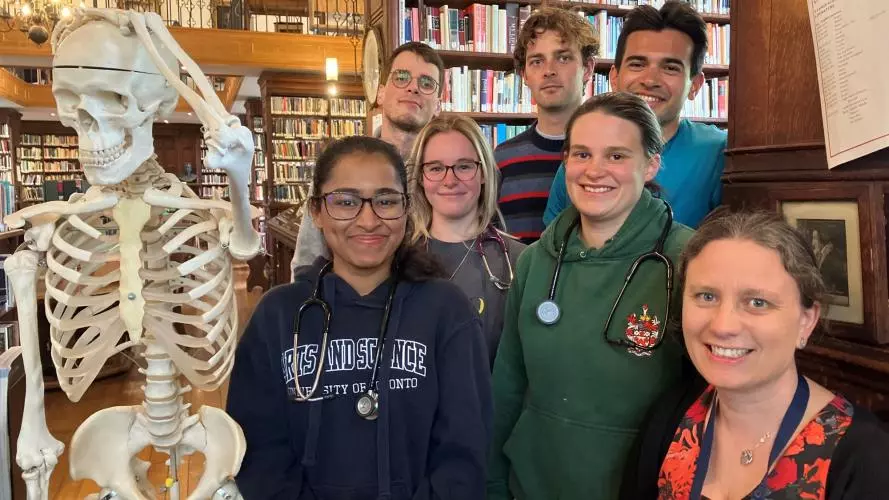 Students with stethoscopes in library next to model skeleton