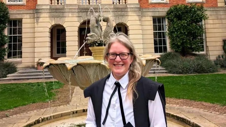 Woman in academic gown in front of a fountain, with building in the background