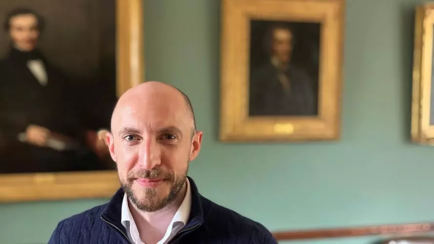 Joe Dollin posing in front of the portraits in the HMC Senior Common Room