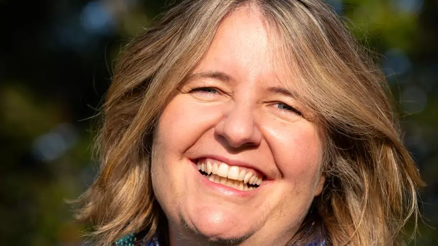 Professor Sophie Park wearing a blue scarff and a black top, posing in front of greenery.
