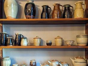 Three shelves of pottery on display in a range of shapes from jugs to teapots to jars.  