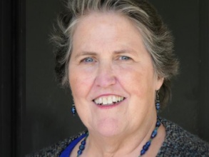 Maureen Oneill wearing blue earrings and necklace, posing in front of a black background.