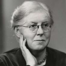 A portrait in black and white of a women with white hair, smiling looking away from the camera.