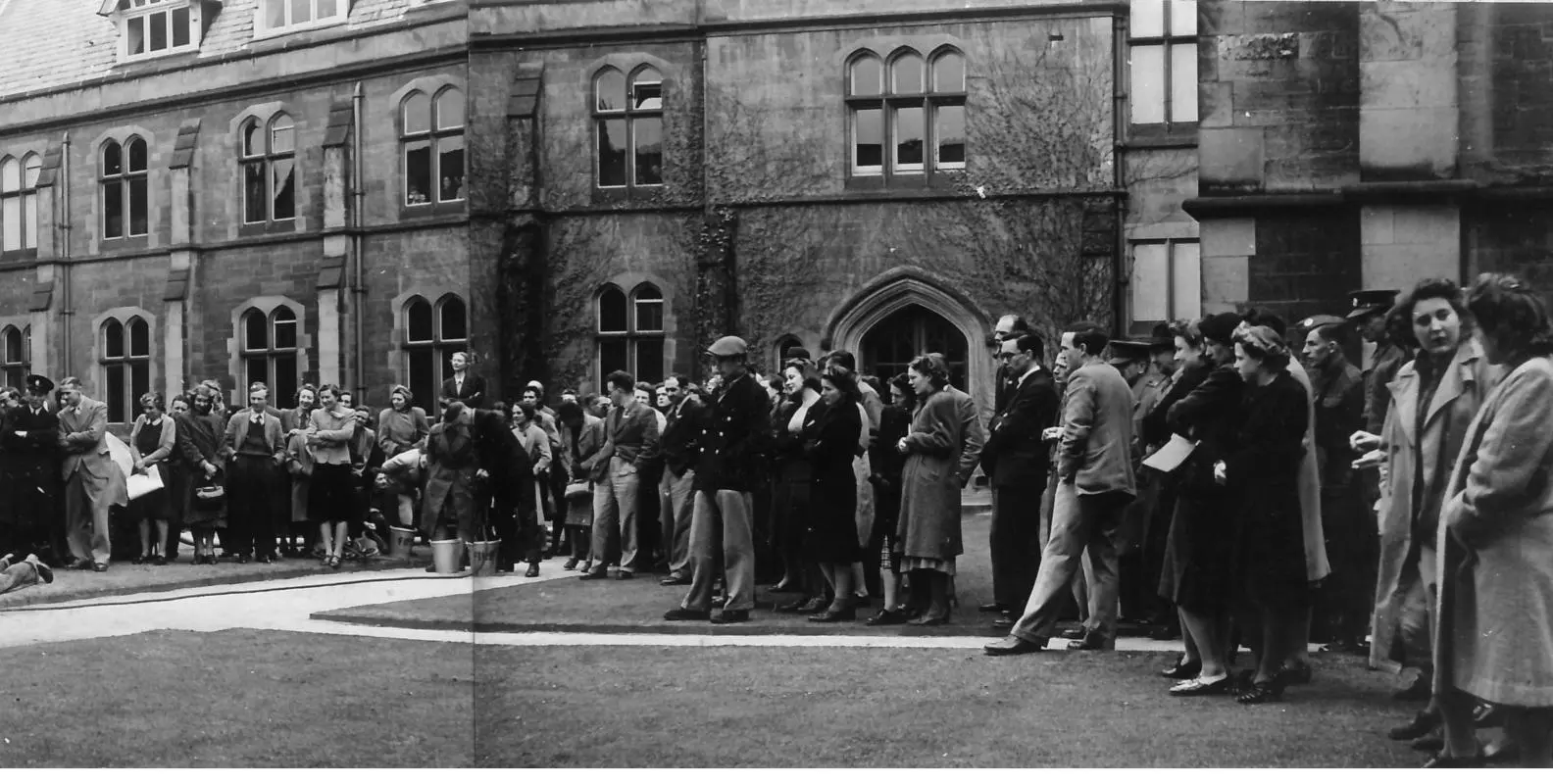 Photograph showing a crowd of people standing in the College quad watching a fire drill beyond the edge of the picture